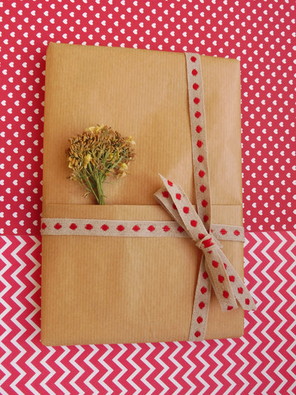Carnet A5 Mystère sur fond rouge et blanc, emballé dans un paquet cadeau de kraft brun, un bouquet de brocoli en fleurs séchées.
