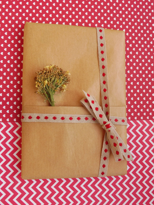Carnet A5 Mystère sur fond rouge et blanc, emballé dans un paquet cadeau de kraft brun, un bouquet de brocoli en fleurs séchées.